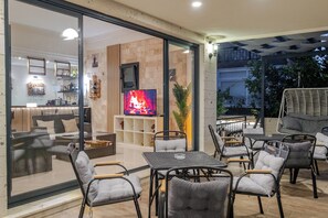 A modern living room with a TV, comfortable seating, and a glass wall overlooking a balcony. - Bayram Hotel (Cesme)