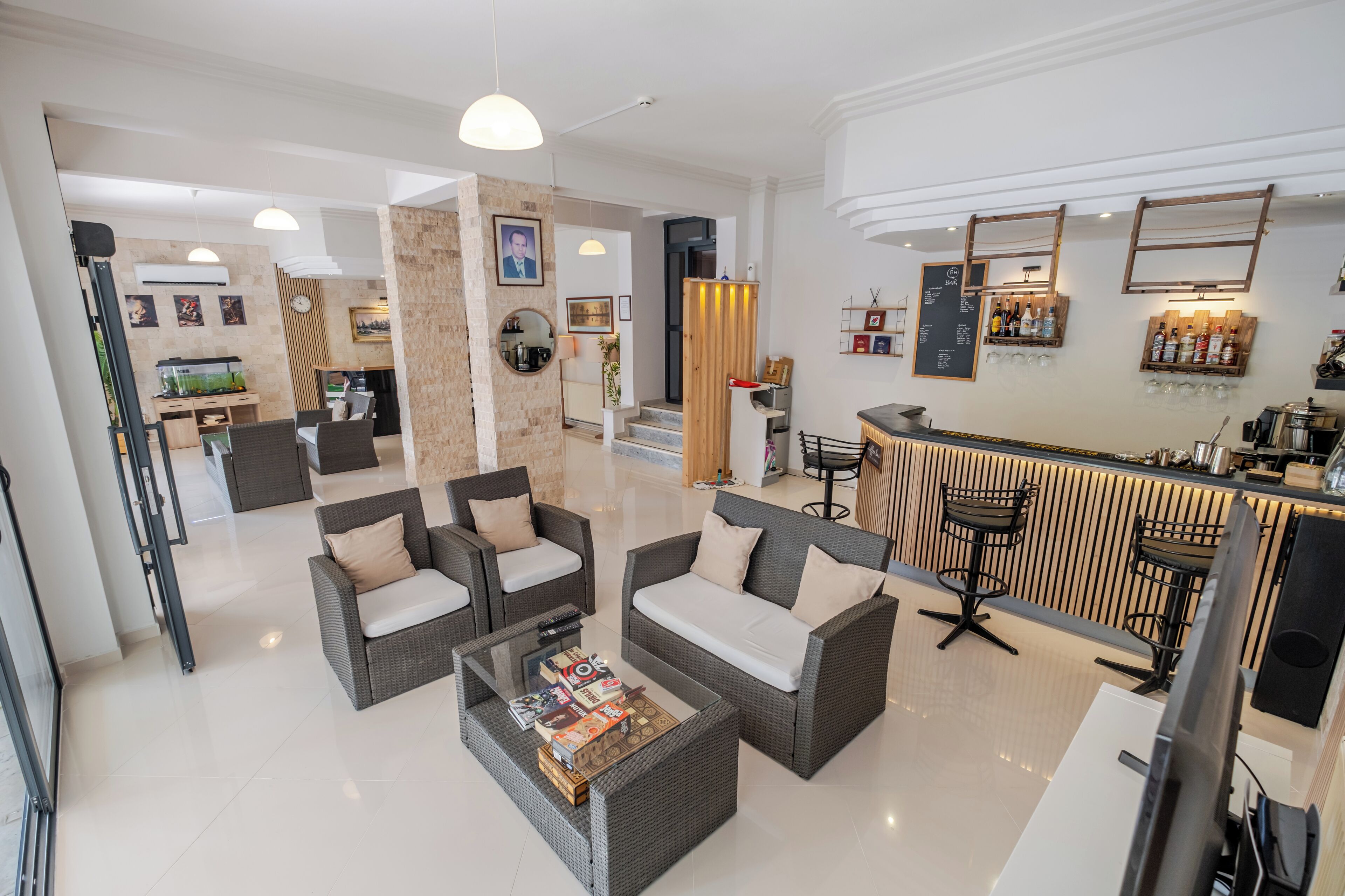 A modern hotel lobby with wicker sofas, a glass coffee table, and a bar area with stools.