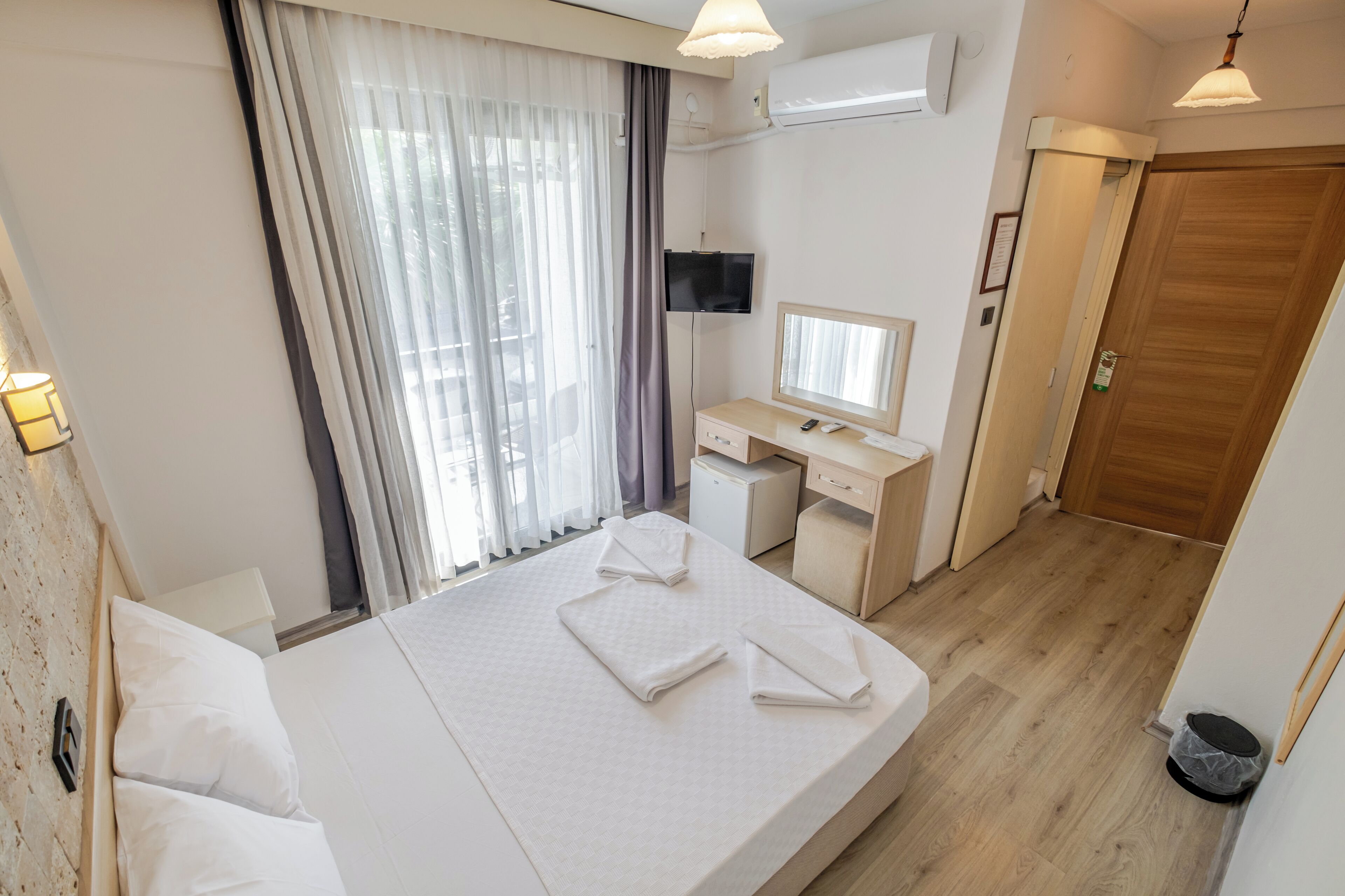 A hotel room with a bed, a desk, a computer, and a TV.