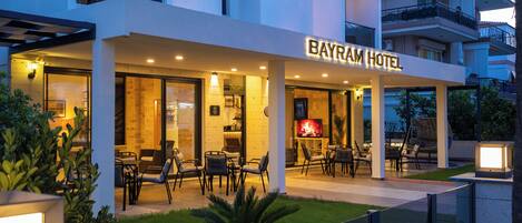 A modern hotel with a well-lit outdoor seating area and a visible TV screen.