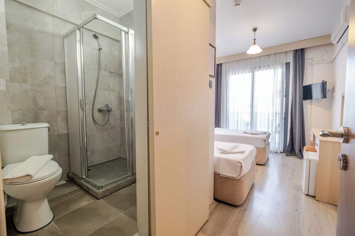 A hotel room with a shower, toilet, bed, bedside table, and a TV mounted on the wall.