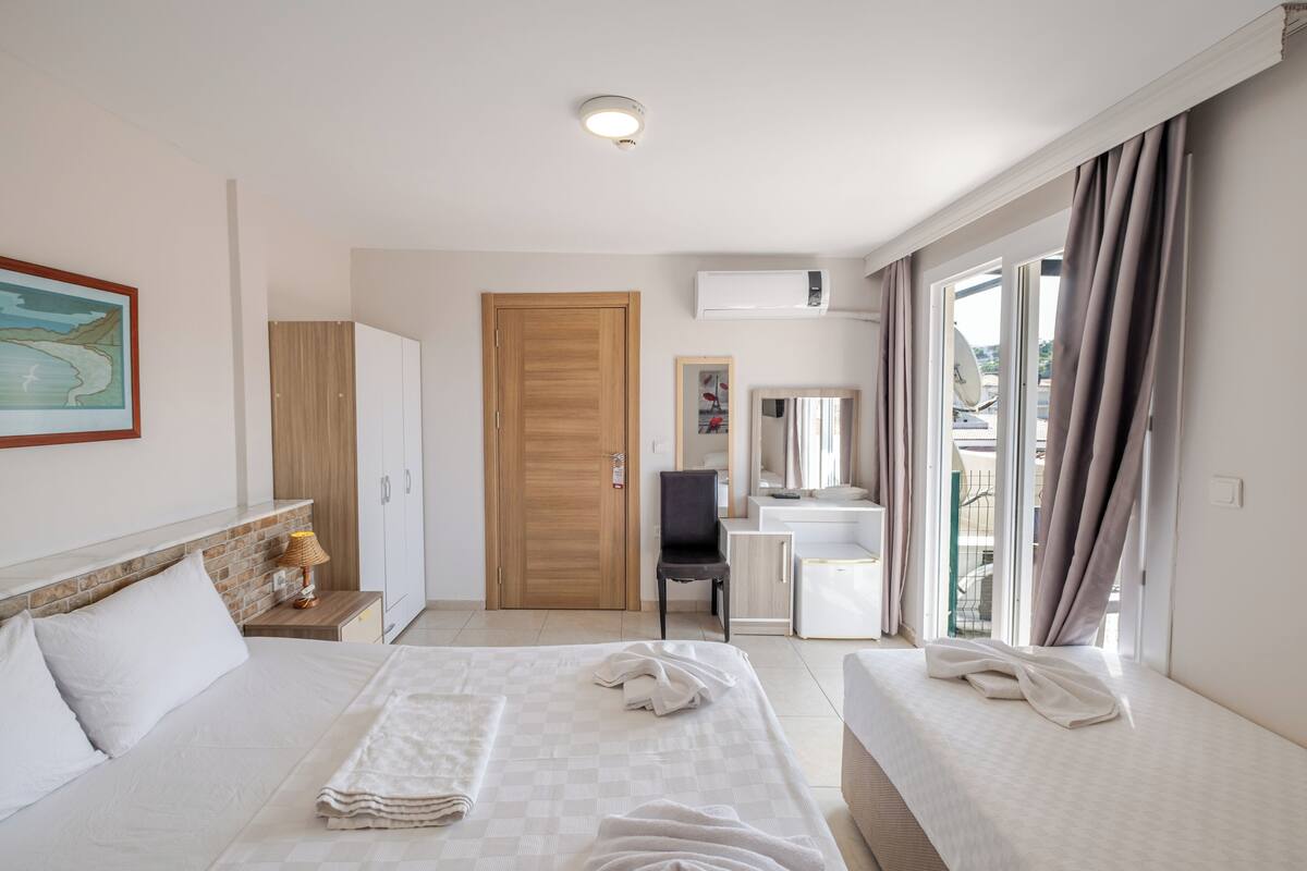 A hotel room with two beds, a wooden door, a bathroom with a mirror, and a view through the window.