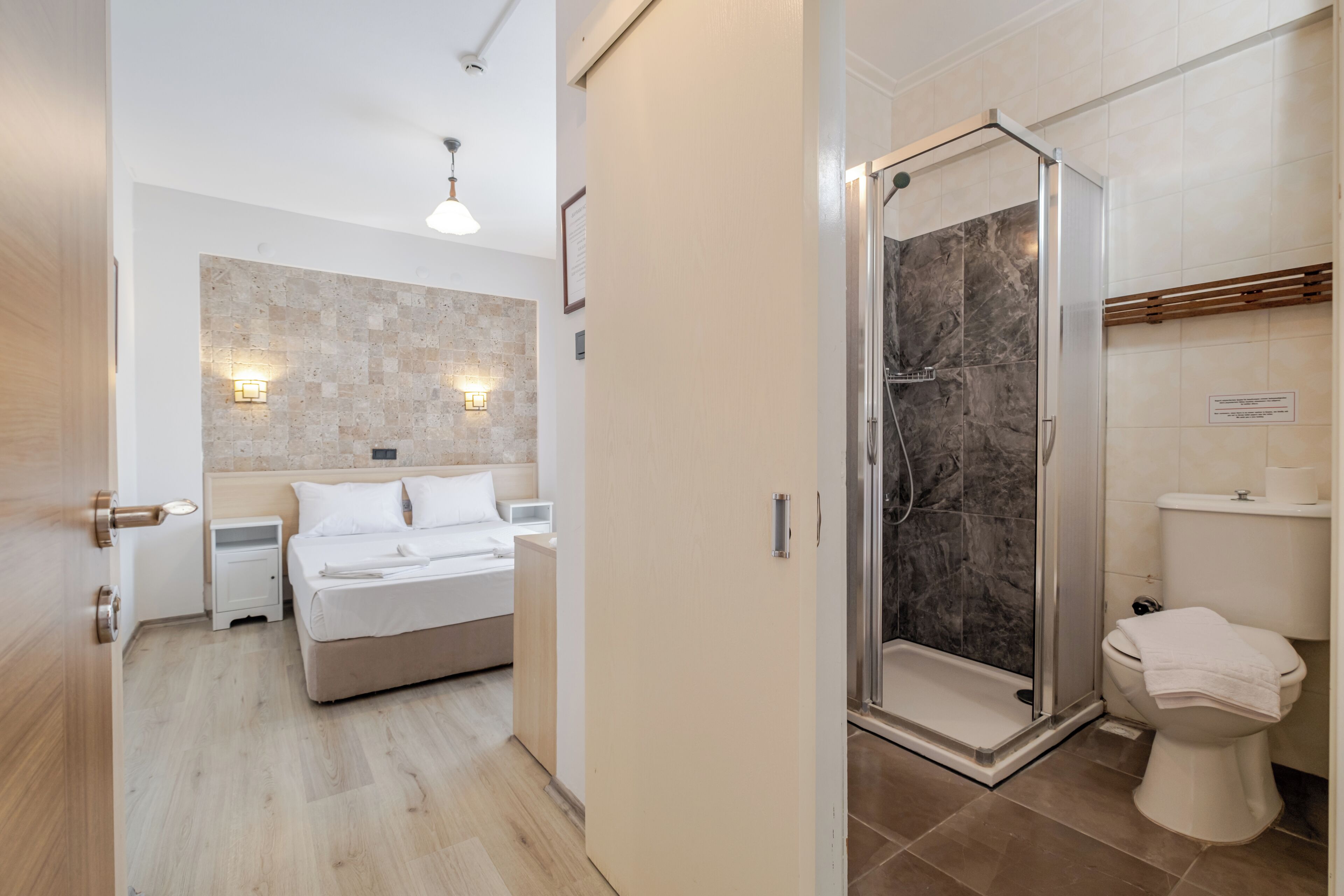 A modern hotel room with a bed, bedside table, and a shower area with a glass door.