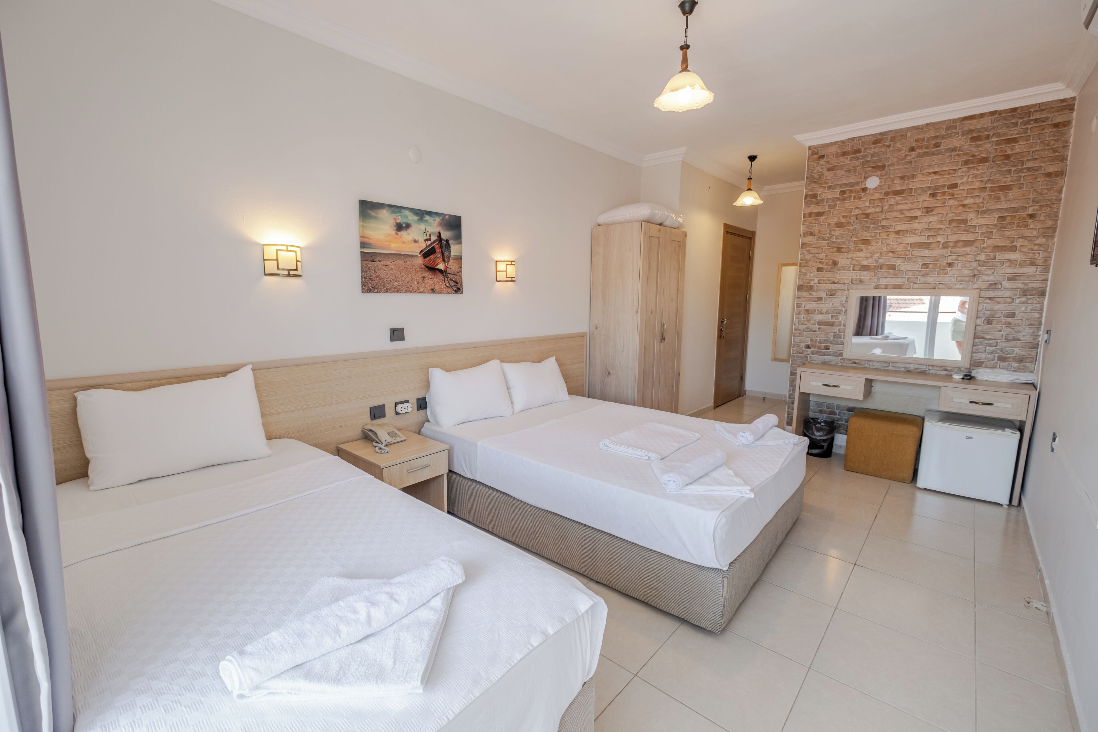 A hotel room with two beds, a desk, a small refrigerator, and a brick wall.