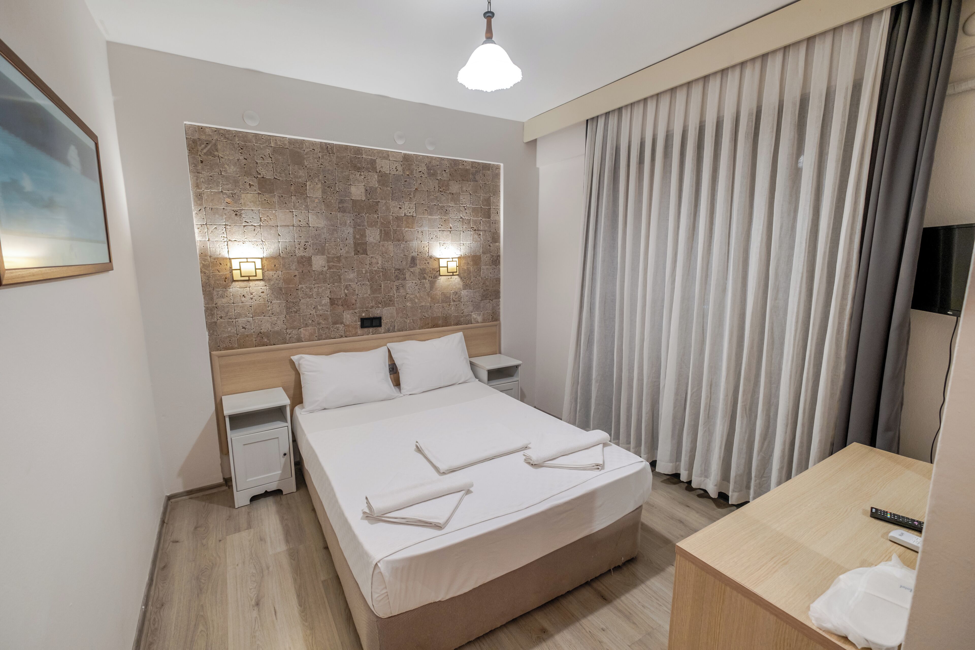 A hotel room with a large bed, bedside tables, a headboard with a textured wall, a TV, and a curtain.