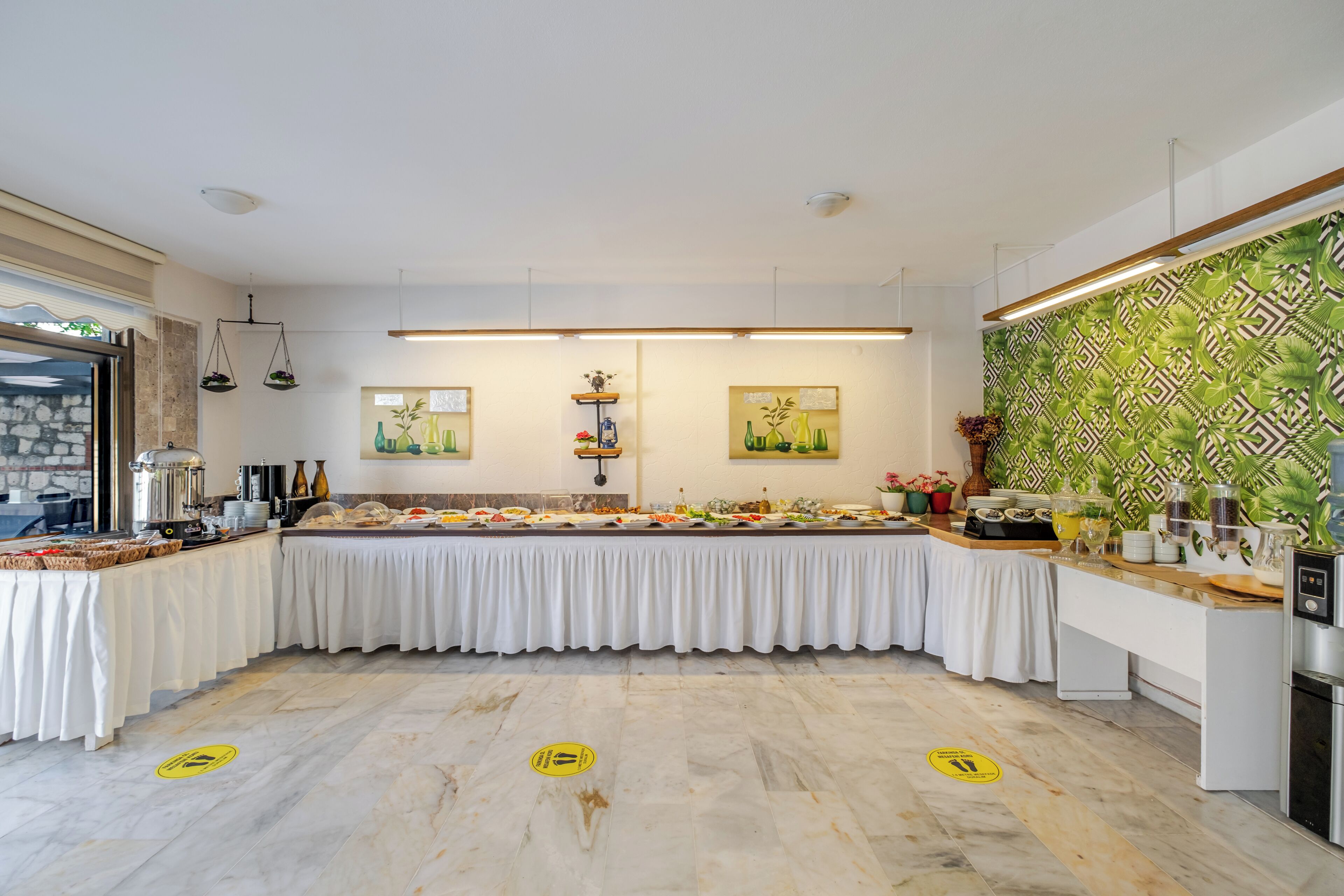 A buffet setup with a variety of food items, a coffee station, and a decorative wall with a tropical pattern.