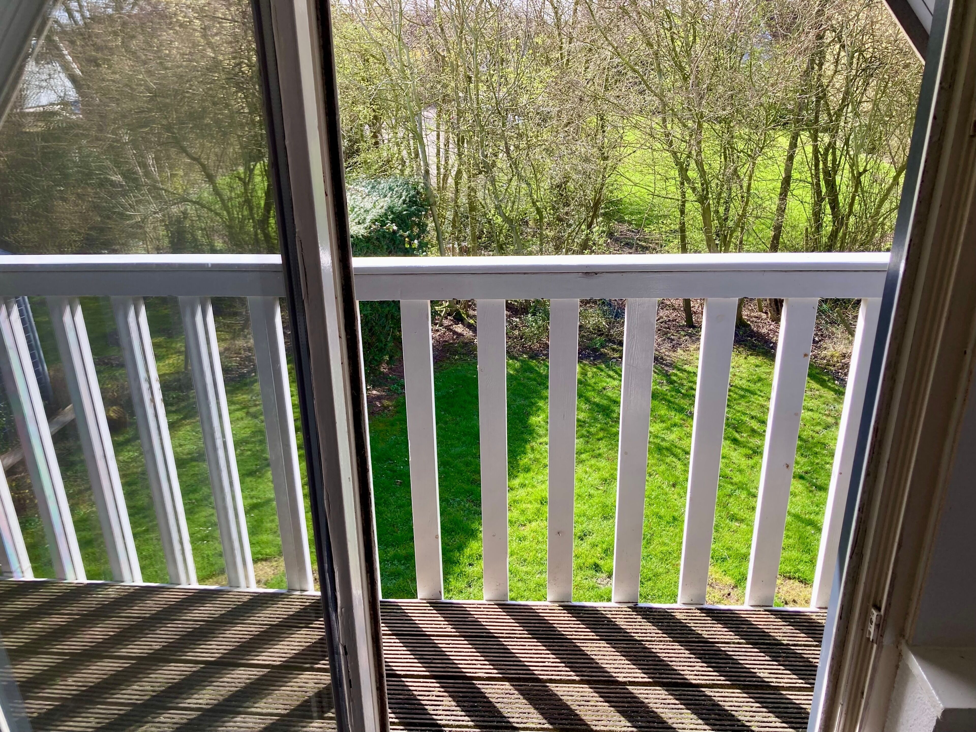 A balcony with a view of a grassy yard and trees.