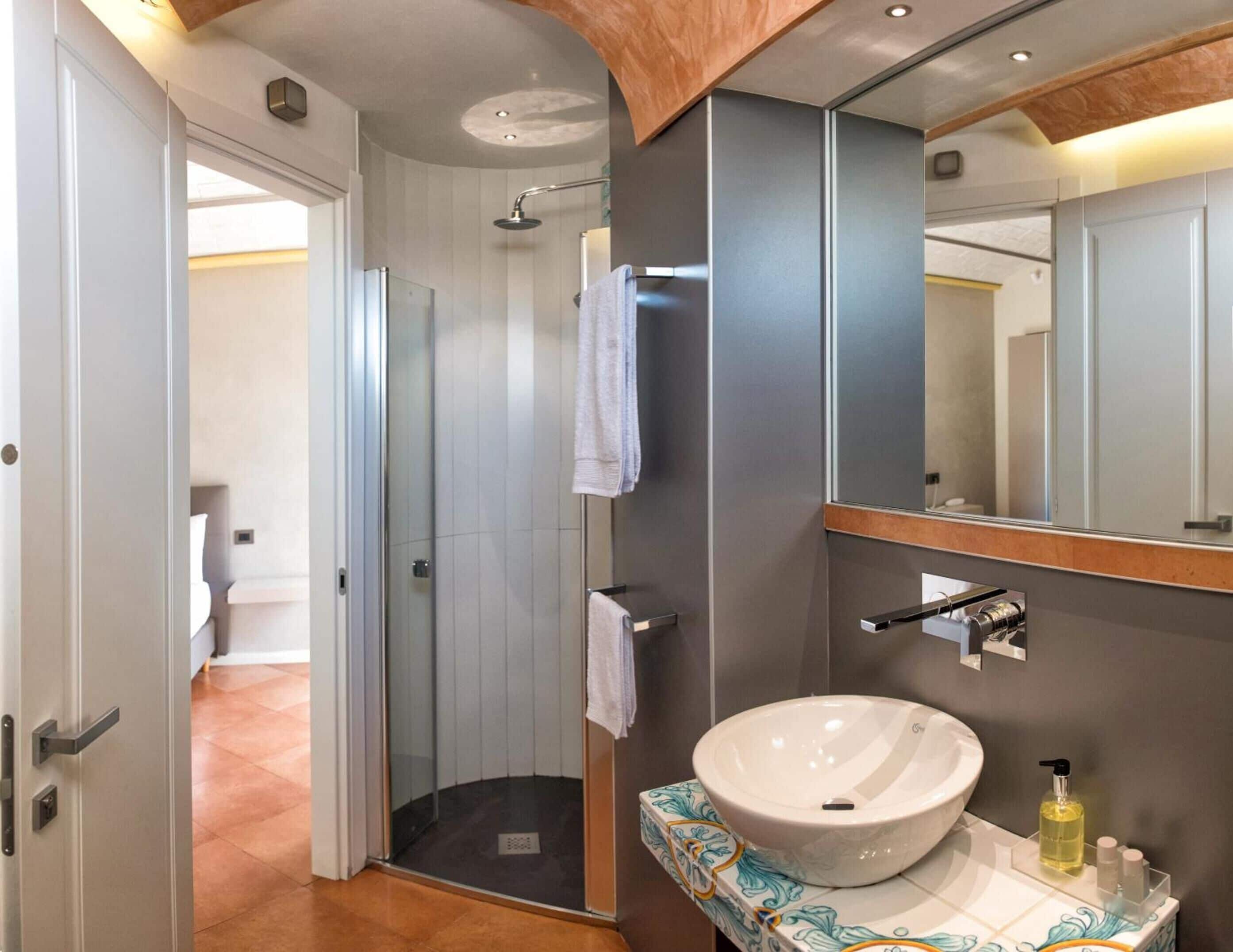 Un baño moderno con un espejo grande, un lavamanos blanco y una ducha.