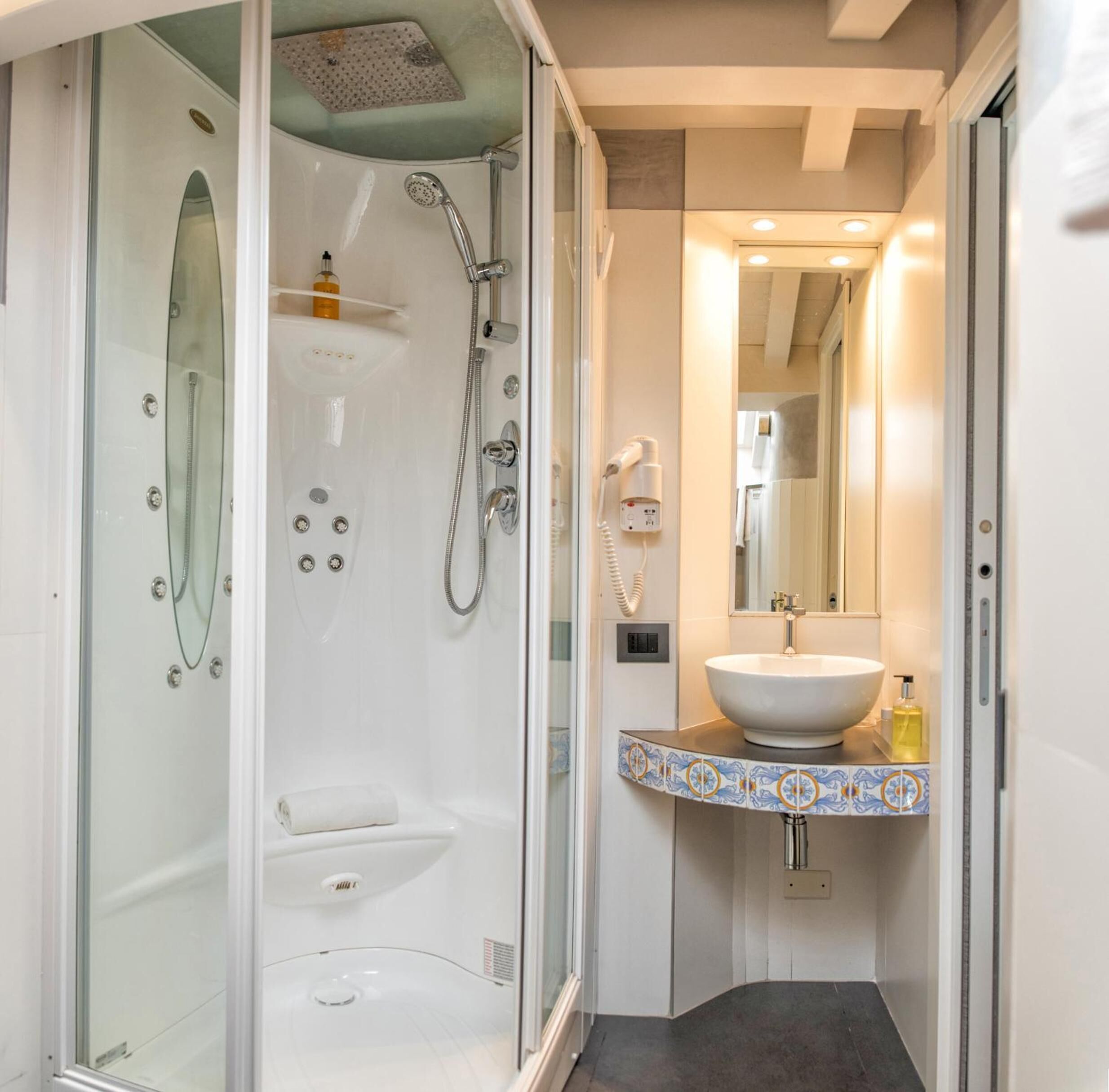 Une salle de bain moderne avec une douche à l’italienne en verre, un lavabo blanc agrémenté d’un pare-feu en mosaïque décorative et un miroir au-dessus du lavabo.