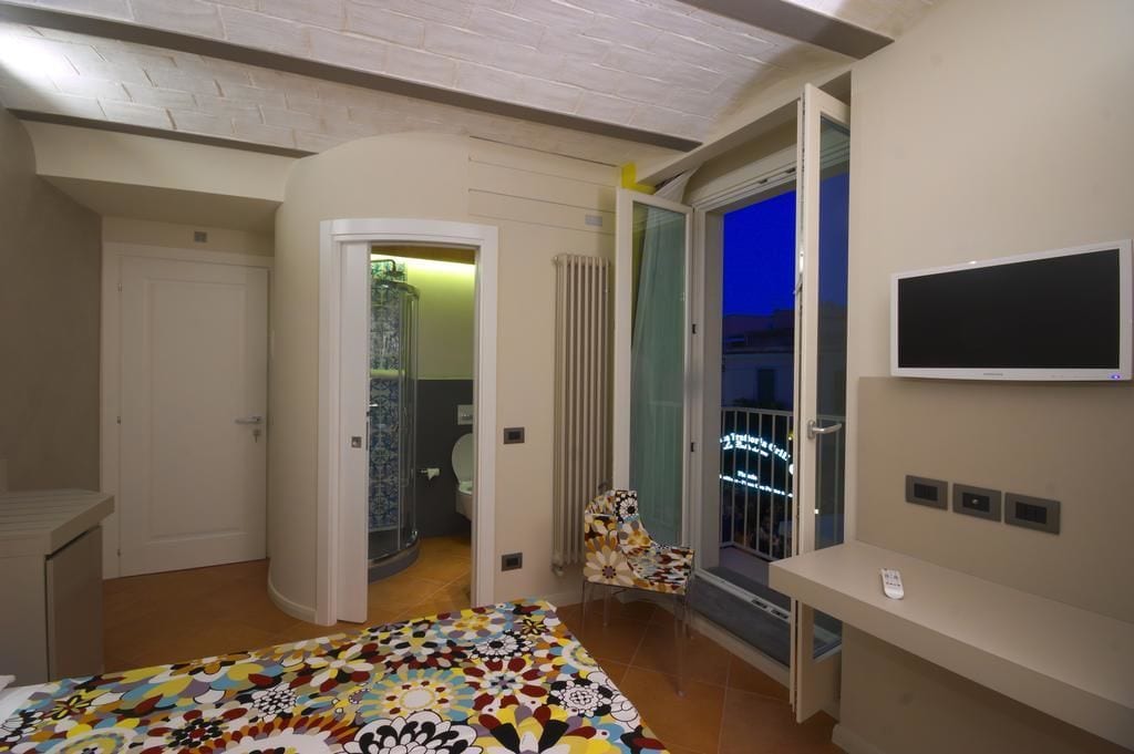 Un dormitorio con cama, televisión, sillón y balcón con vistas.