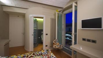 Un dormitorio con cama, televisión, sillón y balcón con vistas.