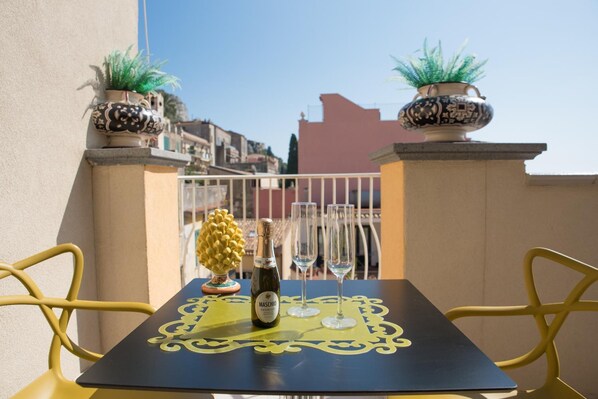 A table with a bottle of Maschio wine, two glasses, and decorative plants on a balcony with yellow chairs. - Casa Turrisi (Taormina)