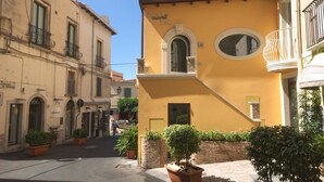A narrow street with buildings on either side, featuring balconies and potted plants. - Casa Turrisi (Taormina)