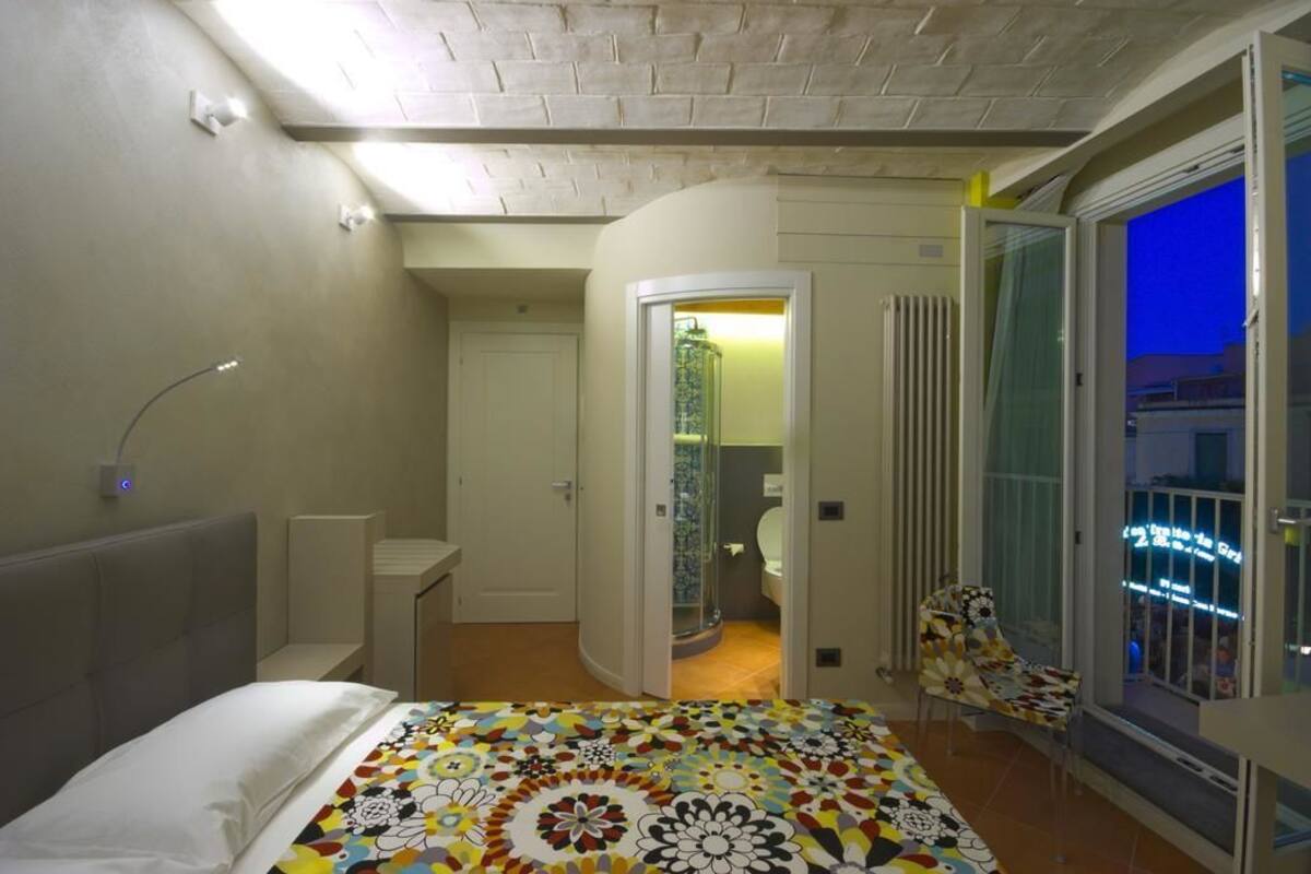 A bedroom with a bed, a chair, a bathroom, and a balcony with a view of the city.