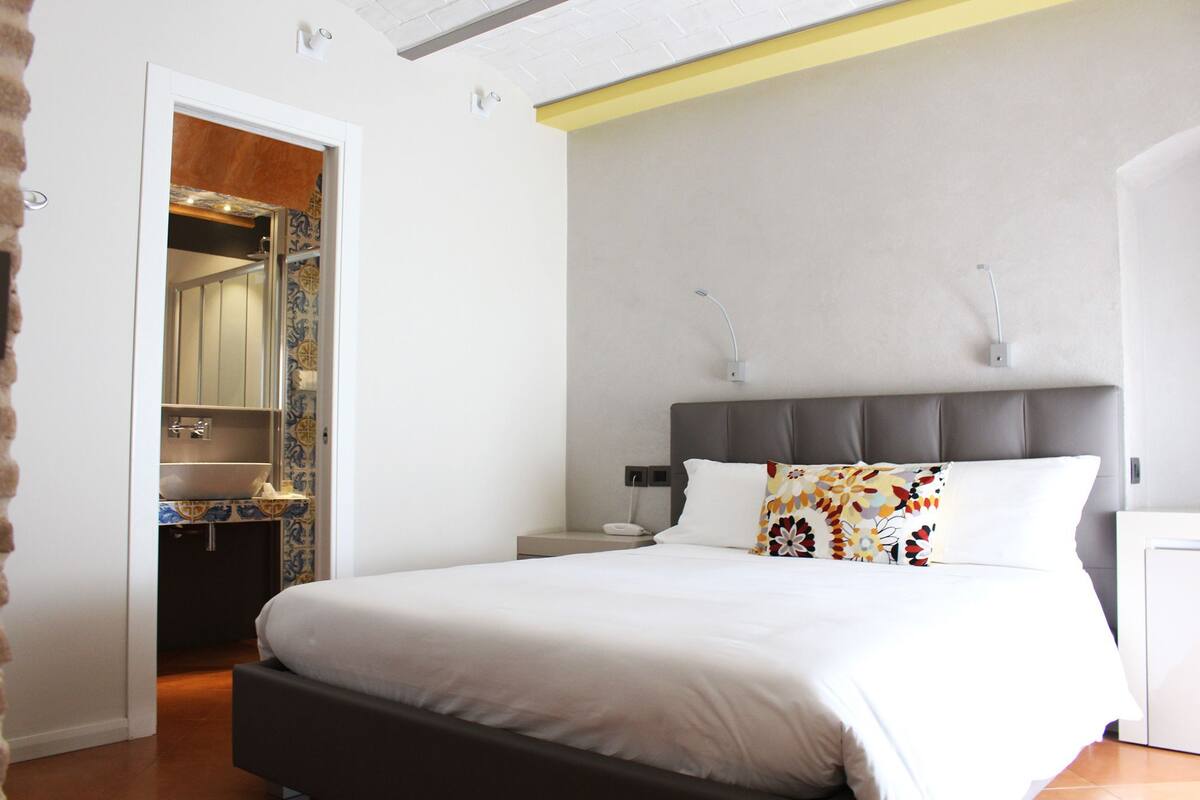 A hotel room with a bed, bedside table, and a bathroom visible through an open door.