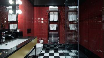 Une salle de bain avec un mur recouvert de carreaux rouges, un sol à carreaux noirs et blancs, un lavabo, des toilettes et une cabine de douche en verre.