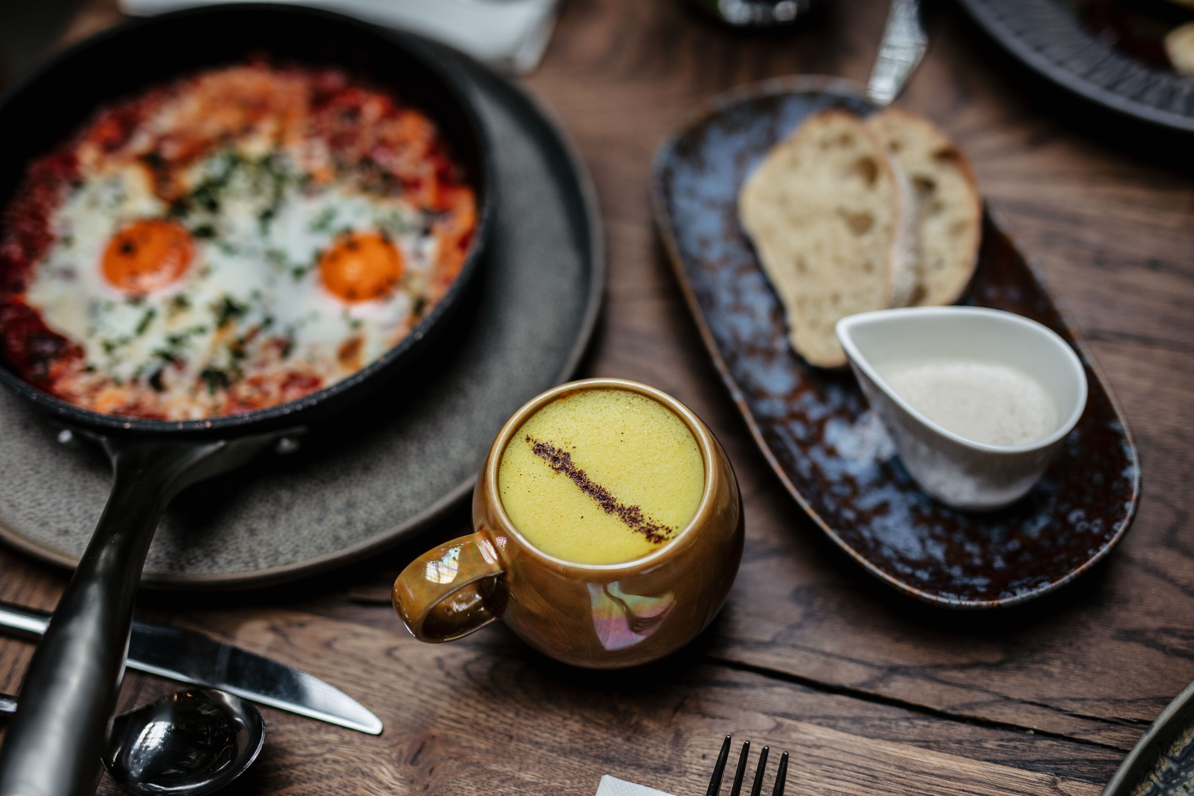 A breakfast setting with a skillet of eggs, a mug of coffee, and a small bowl of sugar on a wooden table.