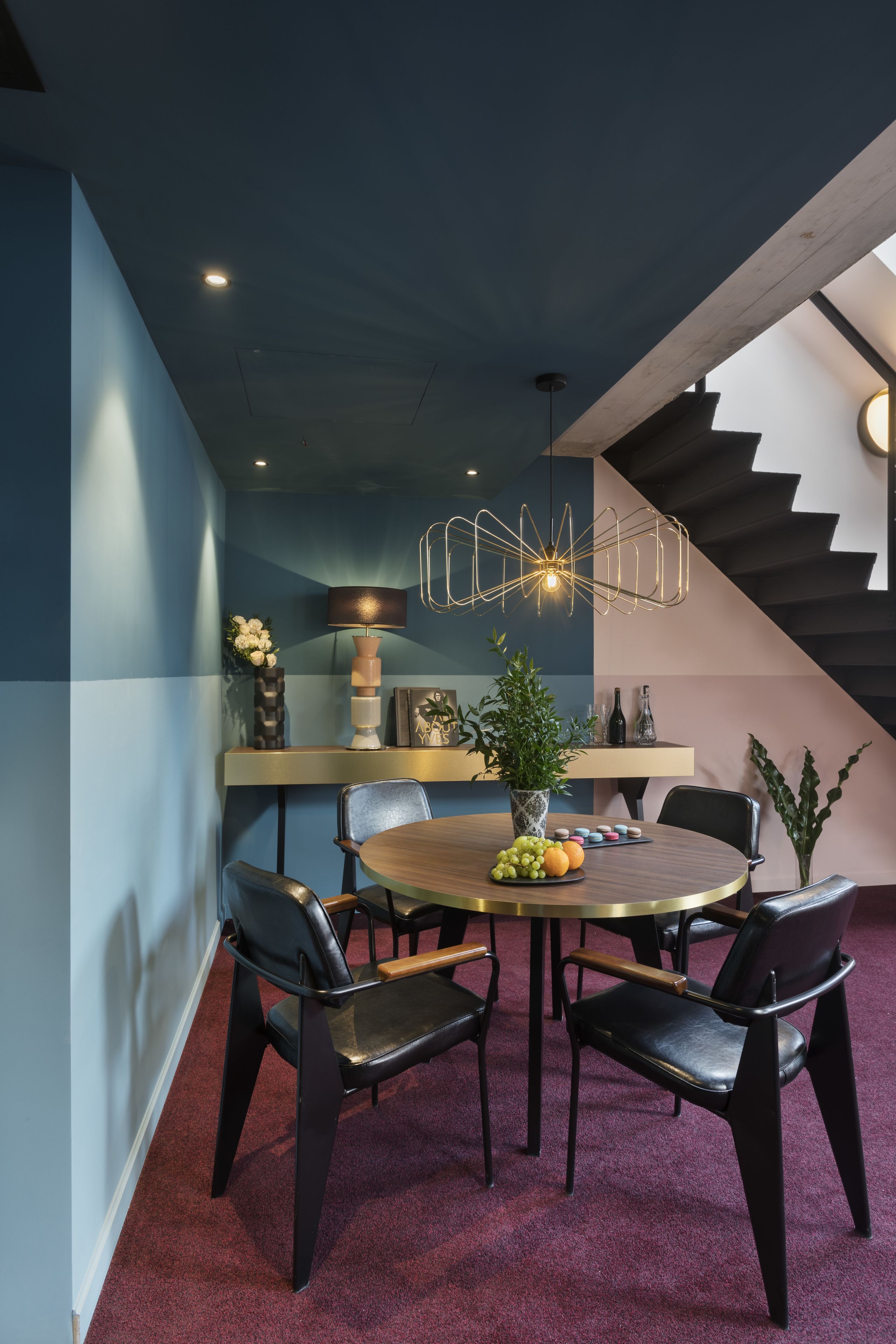 A modern dining area with a round table, black chairs, a vase with flowers, and a pendant light.