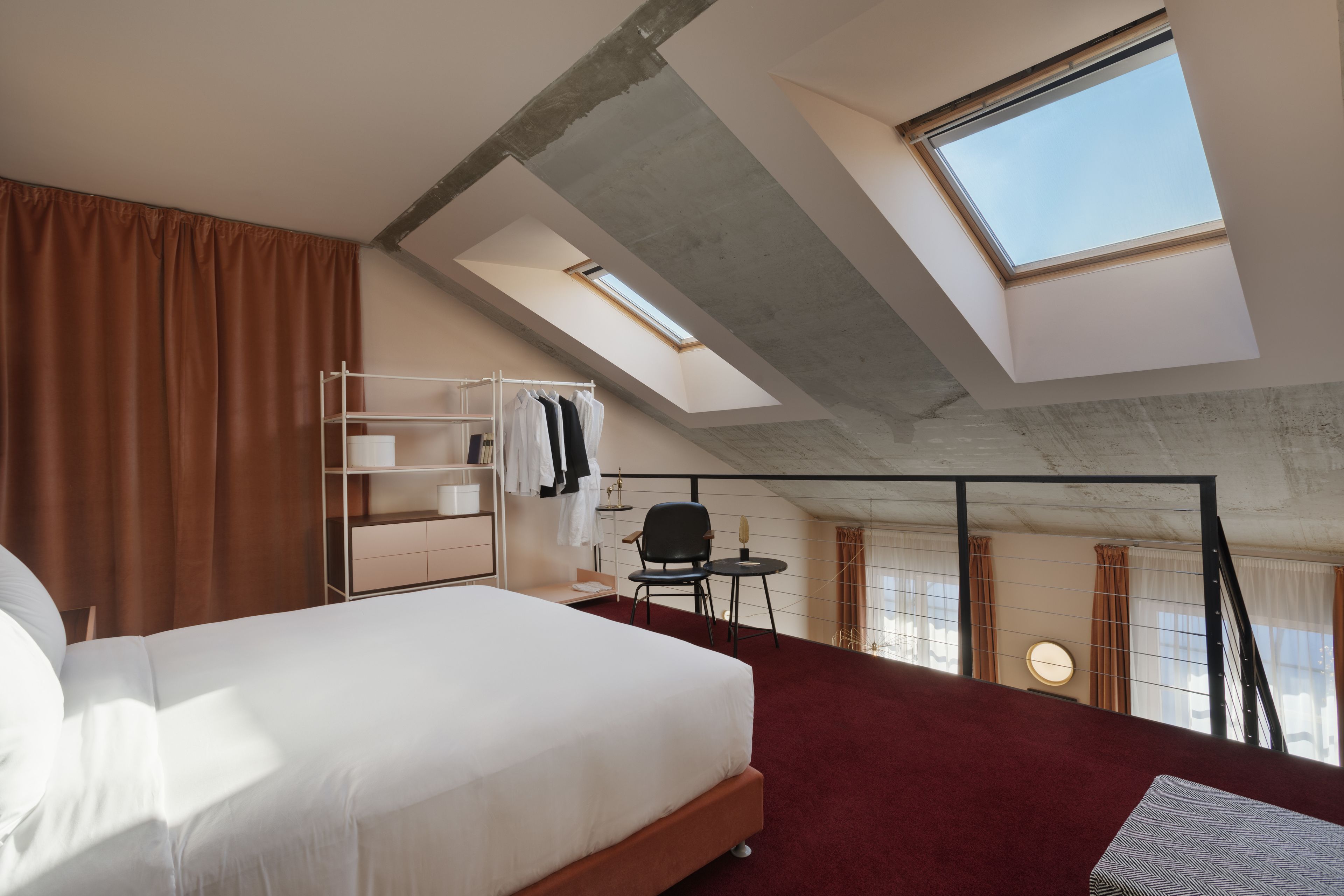 A high-ceilinged room with a skylight, a bed, a desk, and a chair.