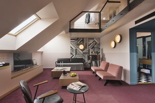 Ένα μοντέρνο διαμέρισμα τύπου loft με τηλεόραση, καναπέ, τραπεζάκι και μια σκάλα που οδηγεί σε ένα μπαλκόνι.