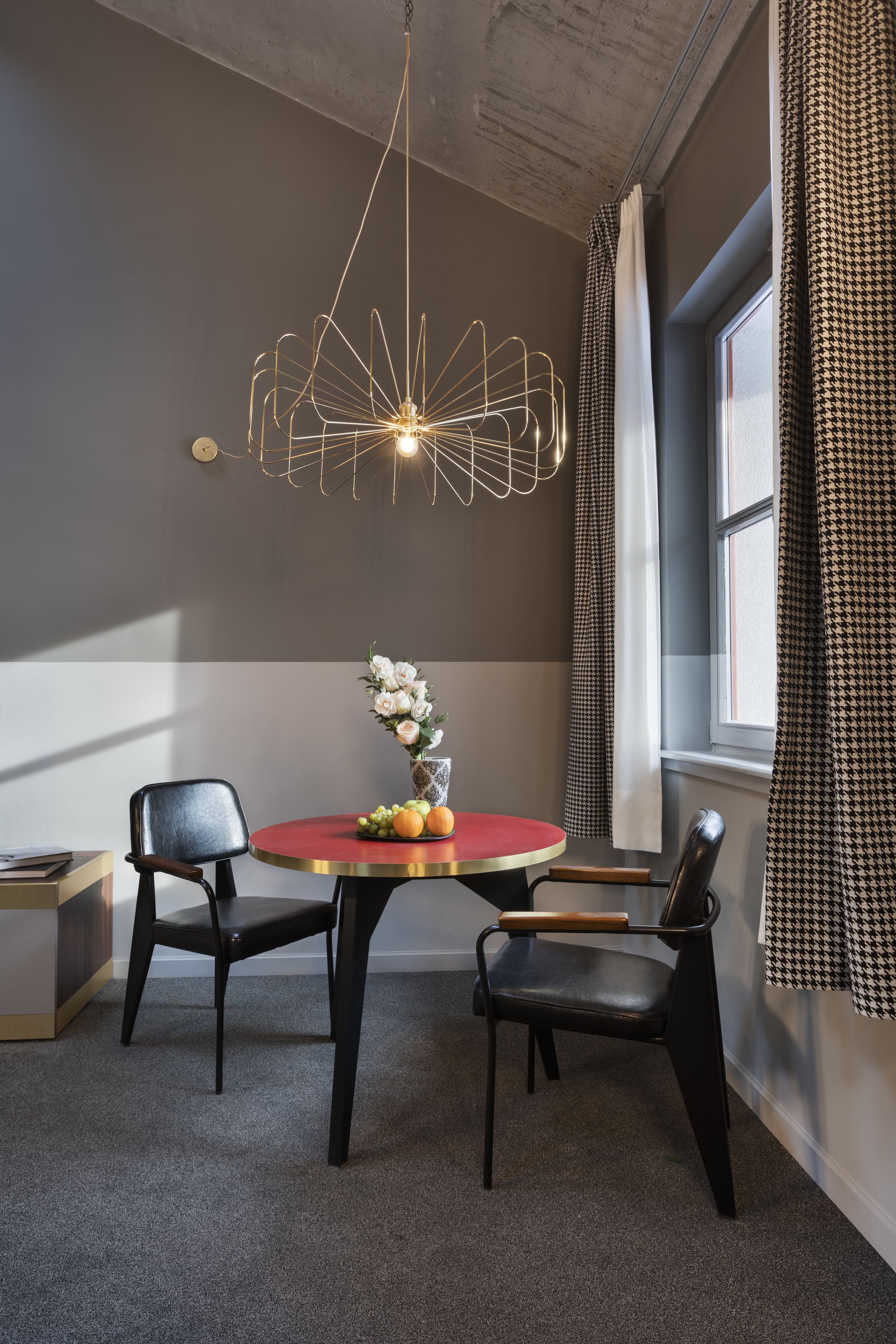 A dining area with a round table, two chairs, a modern chandelier, and a window with curtains.