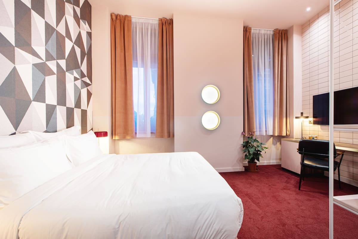 Une chambre d’hôtel avec un grand lit, deux tables de chevet, un bureau avec une chaise, une télévision et une plante en pot.