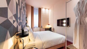 A hotel room with a bed, a desk, a chair, a robe, and a TV.
