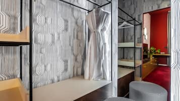 A modern bathroom with a striped wallpaper, a white robe hanging on a rack, a wooden vanity, and a red accent wall.