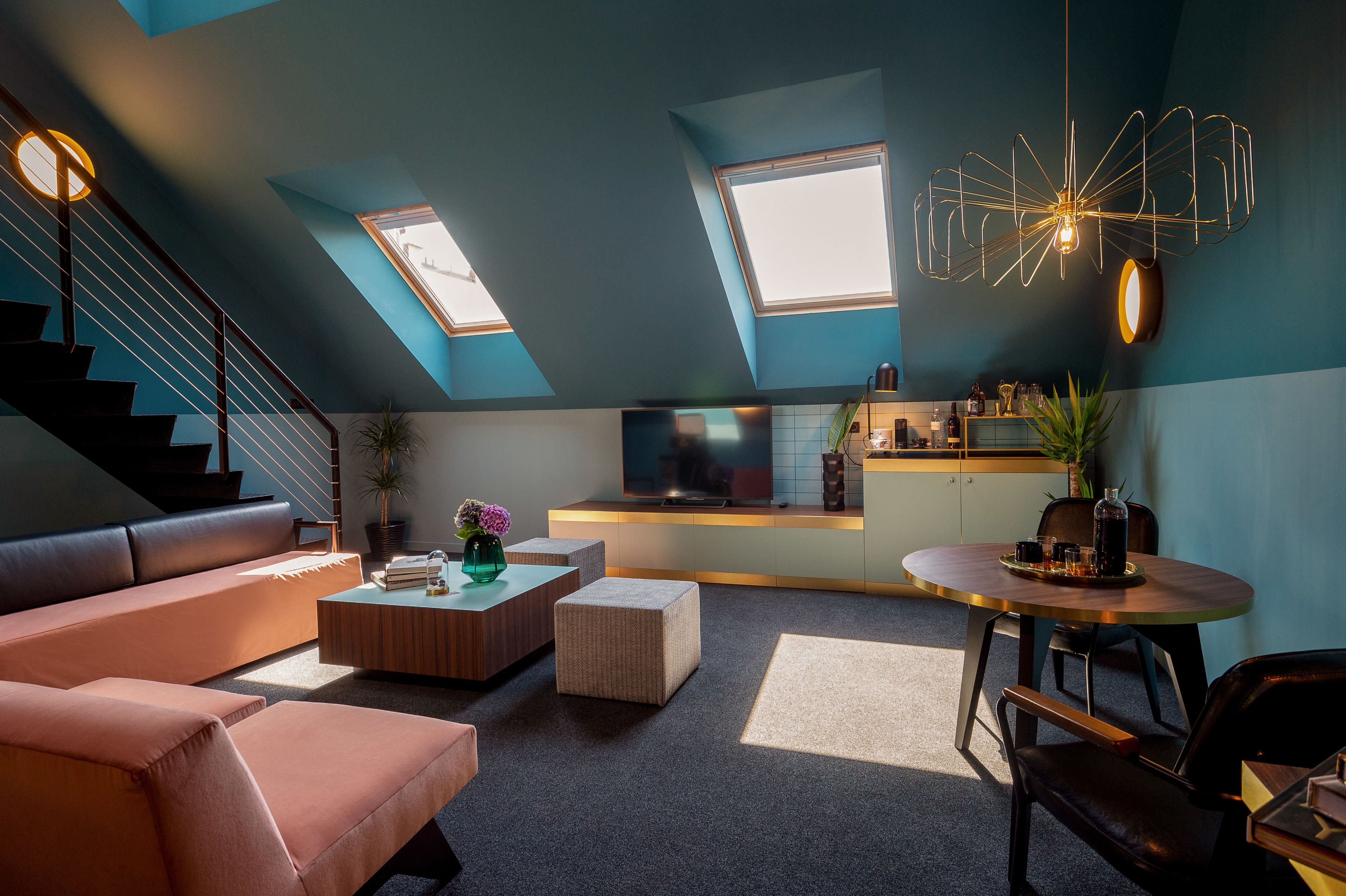 A modern living room with a sofa, coffee table, and a dining area with a table and chairs. There is a TV on a stand, a staircase, and a skylight.