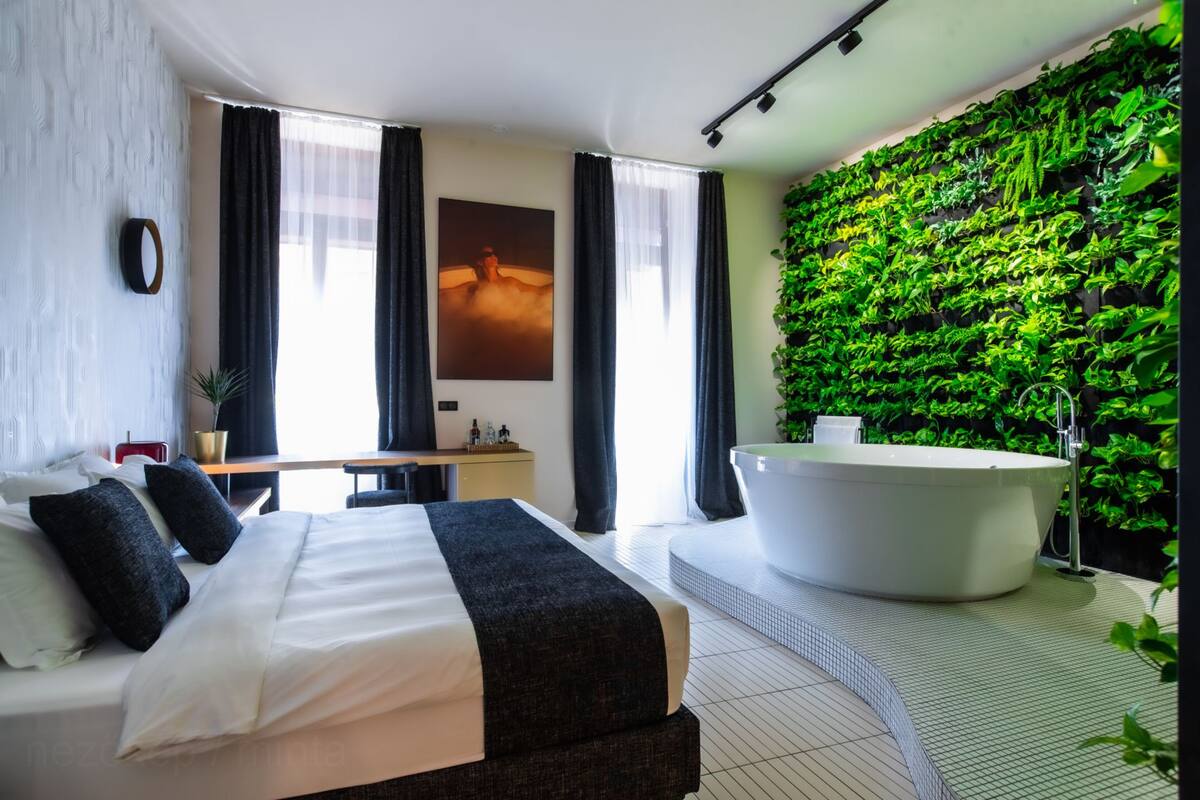 Une chambre d’hôtel moderne avec un grand lit, une baignoire, un mur végétal et une grande fenêtre.