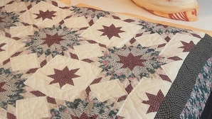 A hotel room with a bed featuring a quilt with star patterns, two pillows with a floral design, and a framed painting of a seascape above the bed. - Ferienwohnung Wittelsbacherstr. 10 -  in ruhiger und zentraler Lage (Bad Reichenhall)