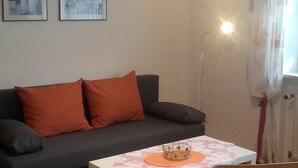 A living room with a grey sofa, orange cushions, a white table with a patterned tablecloth, and a floor lamp. - Ferienwohnung Wittelsbacherstr. 10 -  in ruhiger und zentraler Lage (Bad Reichenhall)