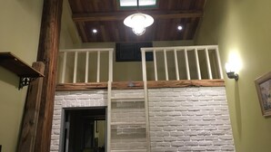 Une pièce dotée d’un espace en mezzanine, avec un mur en briques blanches, des poutres en bois et une rambarde blanche.