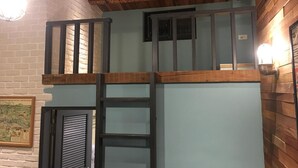 Une pièce de style « loft » avec des poutres en bois apparentes, un lit en mezzanine, une échelle et une carte accrochée au mur.