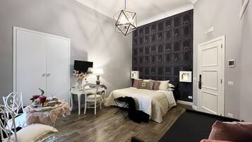 A compact hotel room with a bed, a desk with a chair, a television, and a patterned wall.