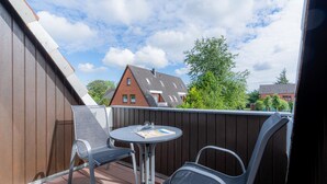 A balcony with two metal chairs and a small round table, overlooking a residential area with houses and trees. - Apartment 5 "Bellmann" (ID 024) - House Dorfstraße 30a (Sankt Peter-Ording)