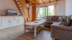 A cozy living room with a wooden staircase, a sofa, a coffee table, and a TV on a cabinet. - Apartment 5 "Bellmann" (ID 024) - House Dorfstraße 30a (Sankt Peter-Ording)