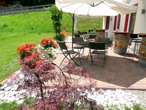 An outdoor patio with brick flooring, black chairs, a white umbrella, and wooden barrels.