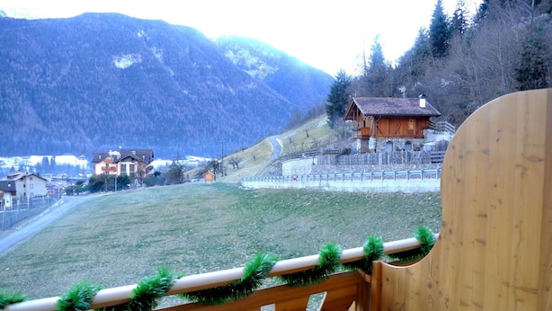 A wooden deck with a view of a mountainous landscape, a small building, and a fenced area. - Agritur Sole Levante (Male)