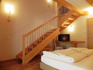 A bedroom with a wooden staircase, a bed with white linens, a television on a wooden stand, and a door.