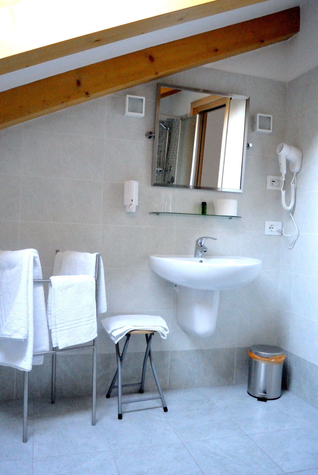 A bathroom with a white sink, a mirror, a hairdryer, a towel rack, and a trash bin.