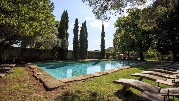 A swimming pool with lounge chairs, surrounded by trees and a stone wall. - Domaine des Escaunes (Sernhac)