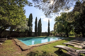 Piscina con sillones de descanso, rodeada de árboles y un muro de piedra.