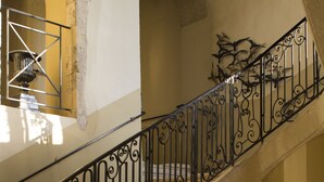A staircase with ornate black metal railings, a cushioned bench, and a vase with flowers on a small table. - Domaine des Escaunes (Sernhac)