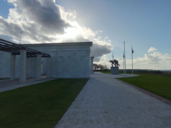 A pathway leading to a building with a covered area and a statue in the distance. - Le Clos Louisiane (Saint-Loup-Hors)