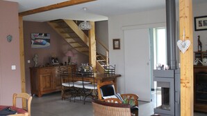 A spacious living area with a wooden staircase, a dining table with chairs, a fireplace, and a view of the outdoors. - Le Clos Louisiane (Saint-Loup-Hors)