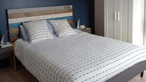 A bedroom with a wooden headboard, a bed with patterned bedding, a nightstand with a lamp, and a wardrobe. - Le Clos Louisiane (Saint-Loup-Hors)