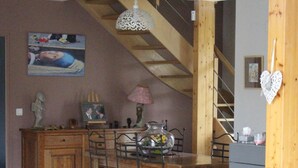 A dining area with wicker chairs, a wooden table, and a staircase in the background. - Le Clos Louisiane (Saint-Loup-Hors)