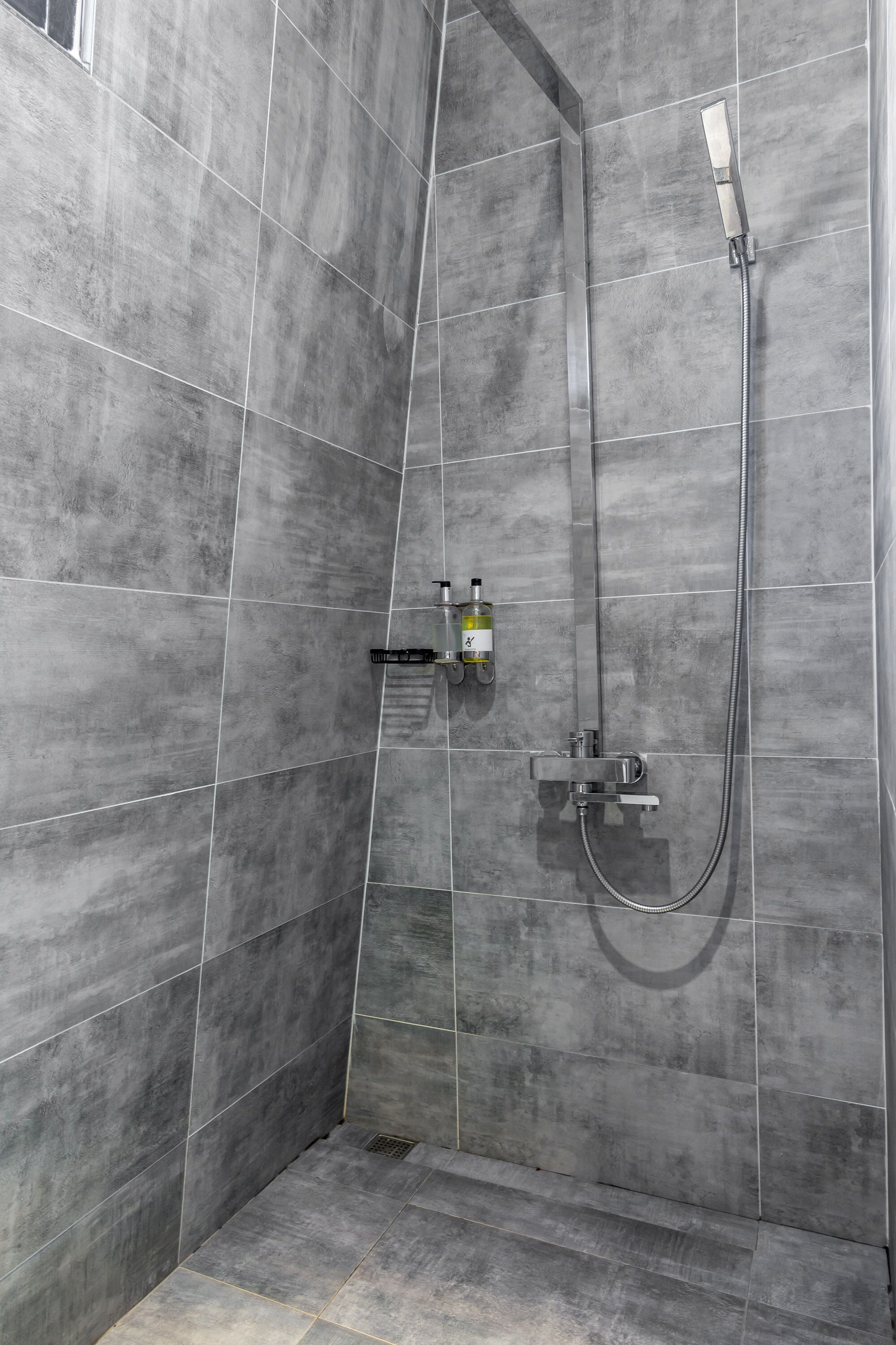 A shower area with grey tiles, a handheld showerhead, and a wall-mounted faucet.