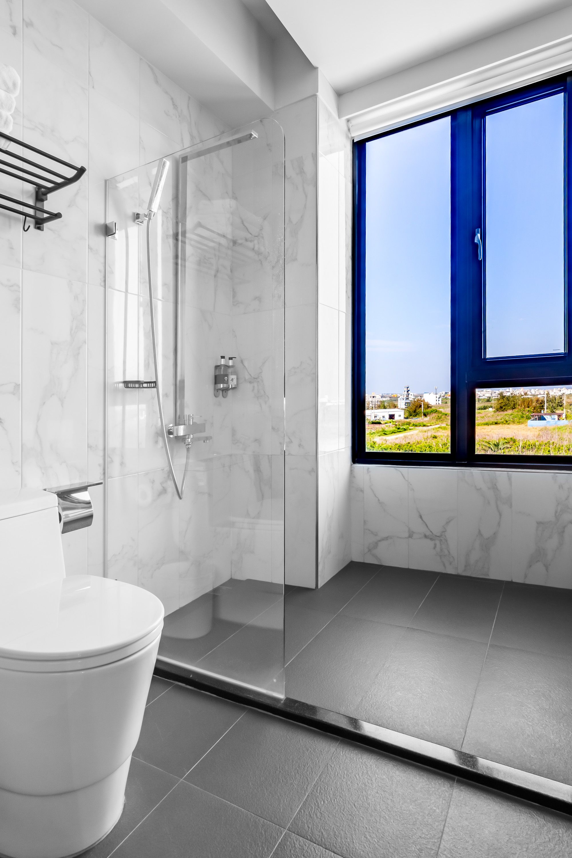 A modern bathroom with a glass-enclosed shower, a toilet, and a large window offering a view of the outdoors.